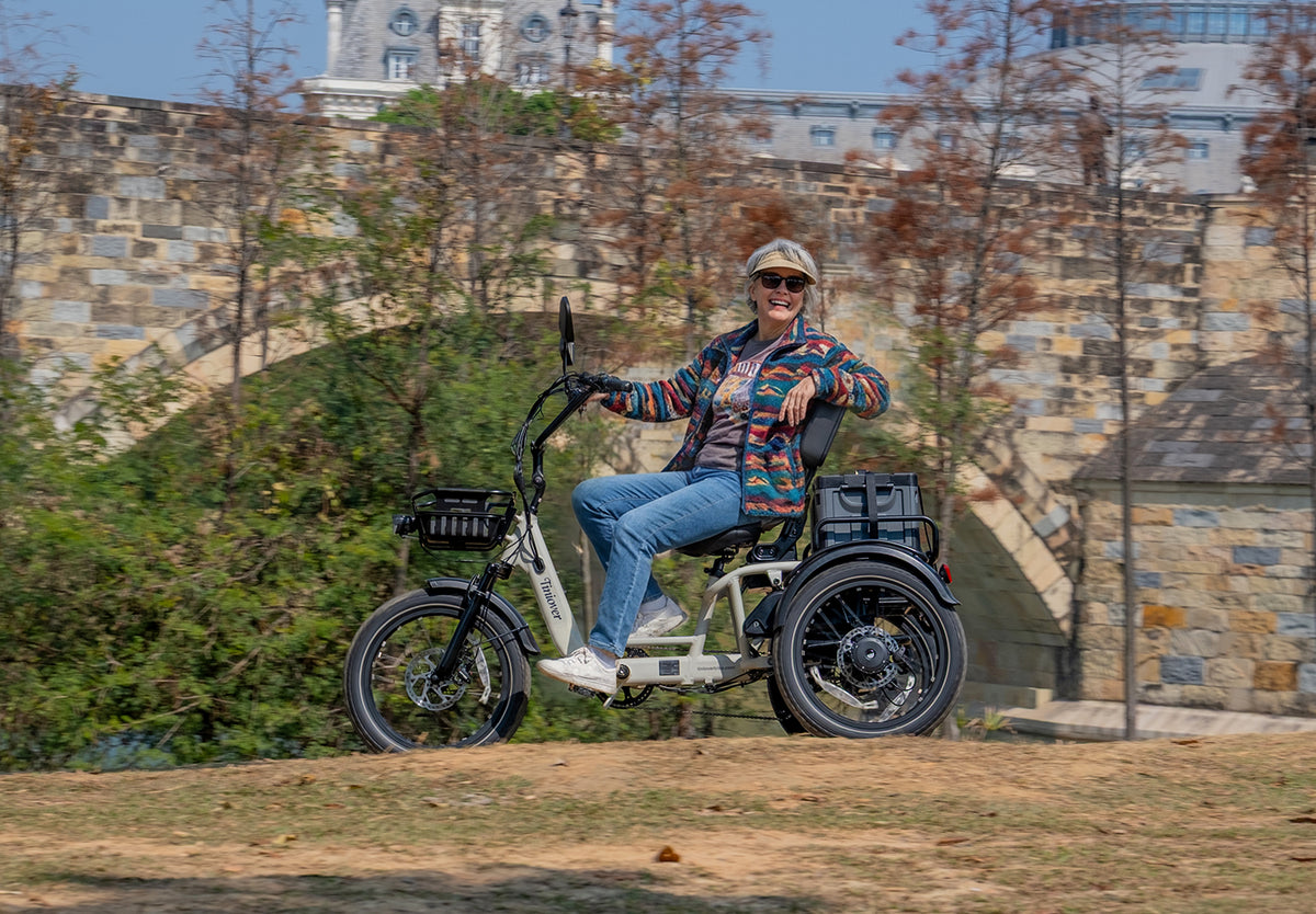 Tiniover River full-suspension electric trike with an adult woman rider on a scenic city path